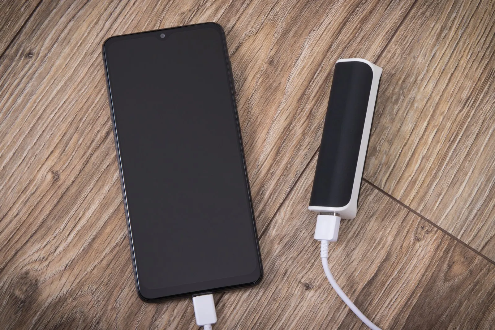 A phone connected by a white cable to a small portable power bank on a wooden surface
