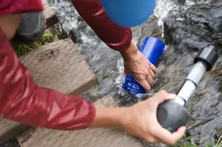 Emergency water filter in use: hands pumping water from a mountain stream