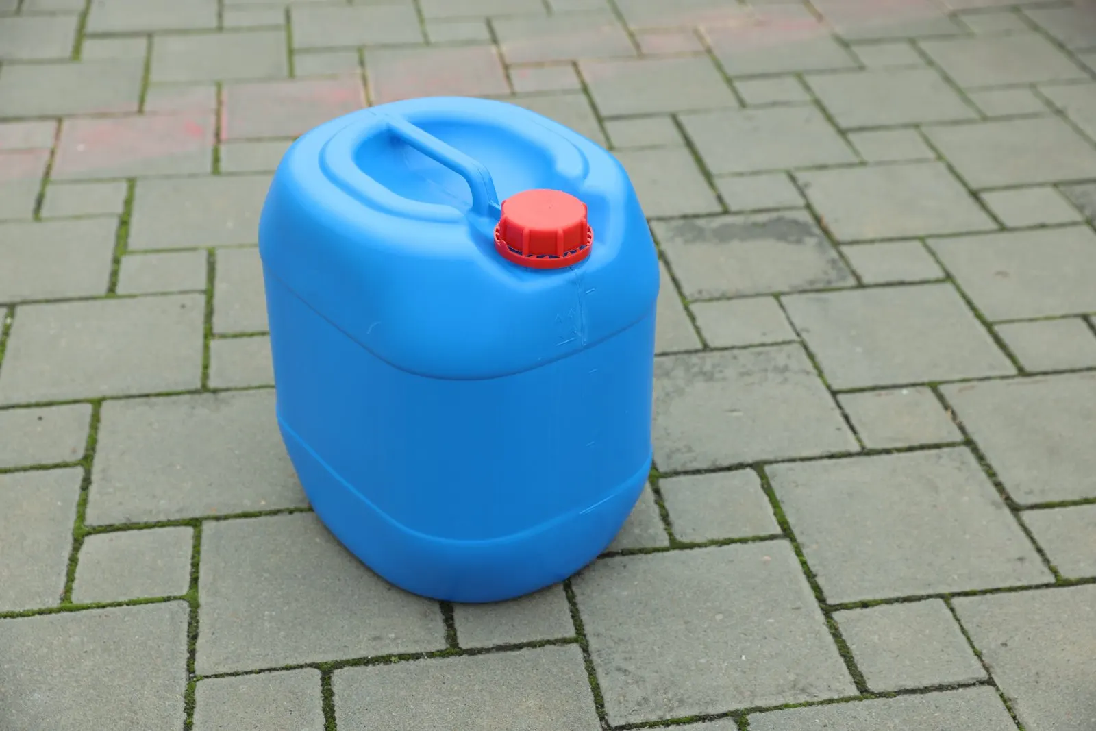 A blue plastic canister with a red cap on paving stones